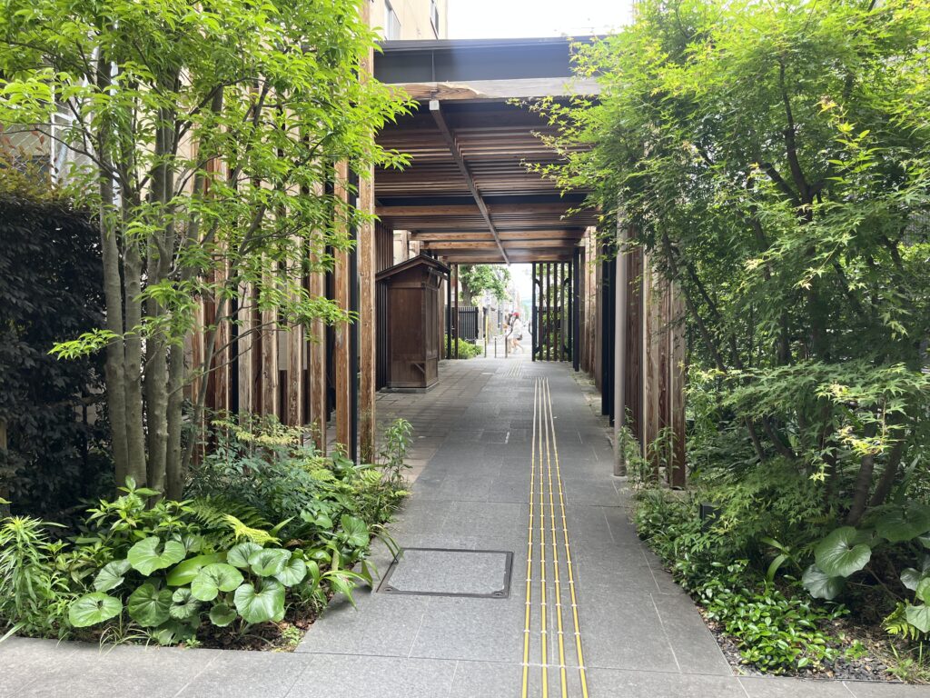 Covered wooden walkway flanked by lush greenery, with a tactile guiding path for pedestrians
