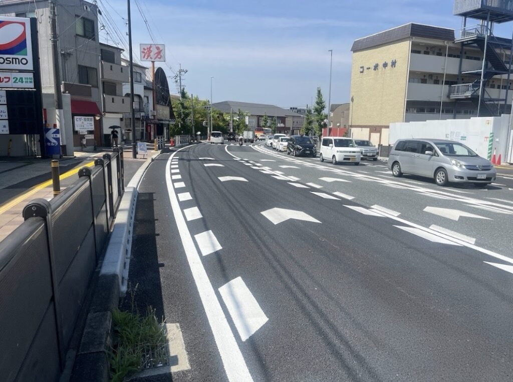 Curved urban street in Japan with several cars and a sidewalk on the left under a clear blue sky.