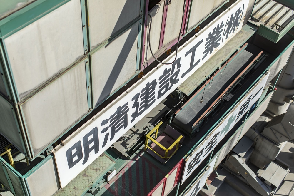 Aerial view of a weathered industrial building with long white banners displaying large Japanese characters on a metal facade.