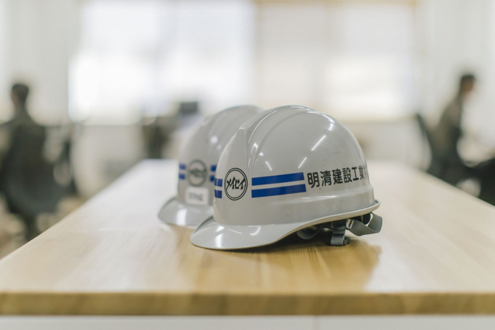 Three gray hard hats with blue stripes lined up on a wooden table in a bright office setting